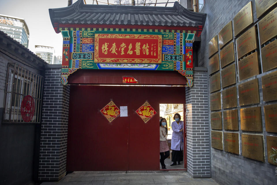 In this March 13, 2020 photo, workers stand at the gates of the traditional Chinese medicine clinic Bo Ai Tang in Beijing, which has been closed to patients during the ongoing coronavirus outbreak. With no approved drugs for the new coronavirus, some people are turning to alternative medicines, often with governments promoting them. (AP Photo/Mark Schiefelbein)