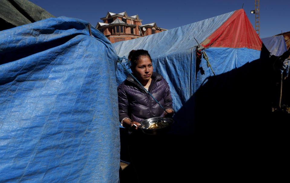 La contorsionista del circo Jumbo, Yhara Gonzales, de 25 años, llevan un plato de papas picadas para cocinar en medio de las carpas del circo cerrado por el COVID-19 en El Alto, Bolivia, el lunes 29 de junio de 2020. (AP Foto/Juan Karita)