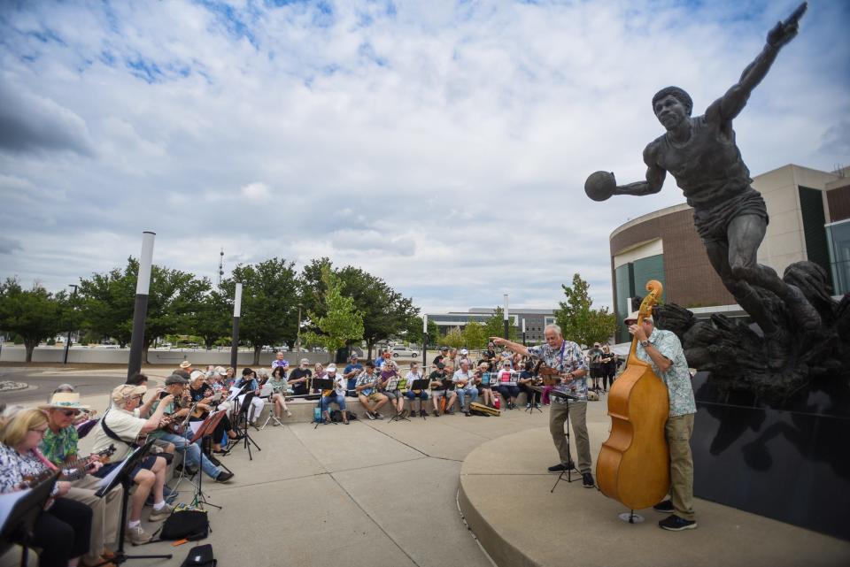 Mighty Uke Day festival founder Ben Hassenger (pointing) and The Ukulele Kings bassist Steve Szilagyi lead a flash mob of ukulele enthusiasts in the song "Do You Believe in Magic" on Friday, June 23, 2023, at the  Magic Johnson statue at the Breslin Center in East Lansing. The flash mob kicked off the 13th annual Mighty Uke Day ukulele festival. The three-day event features workshops, performances, and open jam sessions.