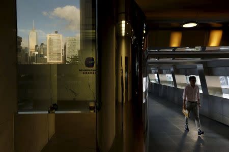 A man walks outside the Hong Kong Exchange as the skyline is seen reflected in the building, in Hong Kong, China June 26, 2015. REUTERS/Bobby Yip