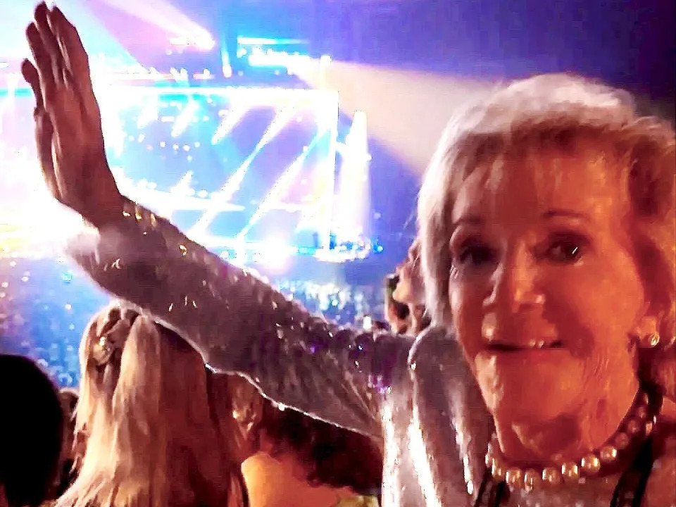 A woman in her late 80s waving at a Taylor Swift concert