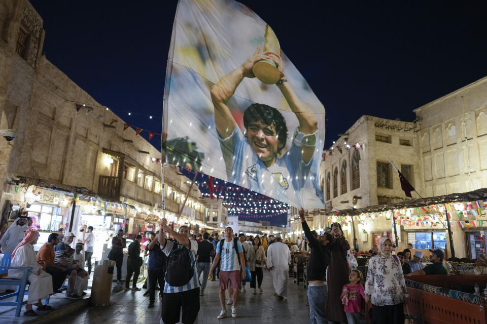 A fan of Argentina waves a flag with the image of late Argentinean soccer star Diego Maradona in Souq Waqif market in Doha, Qatar, Thursday, Dec. 15, 2022. Argentina will face France in the World Cup final match on Dec. 18. (AP Photo/Andre Penner)