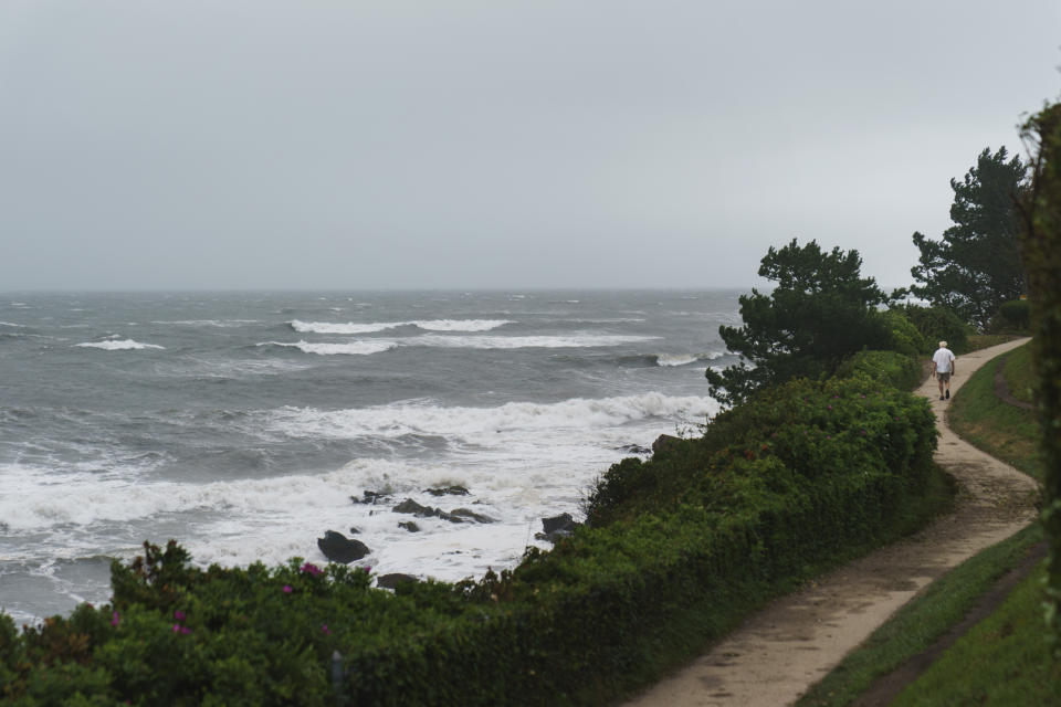 A pedestrian walks along the Cliff Walk as Tropical Storm Henri moves through the area in Newport, R.I., Sunday, Aug. 22, 2021. (AP Photo/David Goldman)