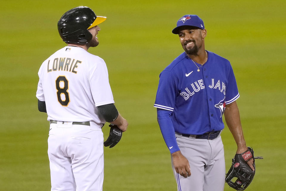 Toronto Blue Jays shortstop Marcus Semien, right, smiles at Oakland Athletics' Jed Lowrie (8) after Lowrie hit a double during the sixth inning of a baseball game in Oakland, Calif., on Monday, May 3, 2021. (AP Photo/Tony Avelar)