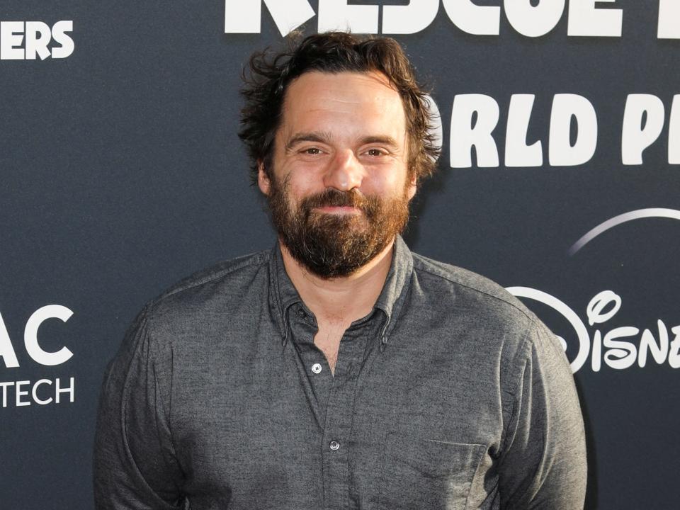 Jake Johnson wears a gray shirt and in front of black background
