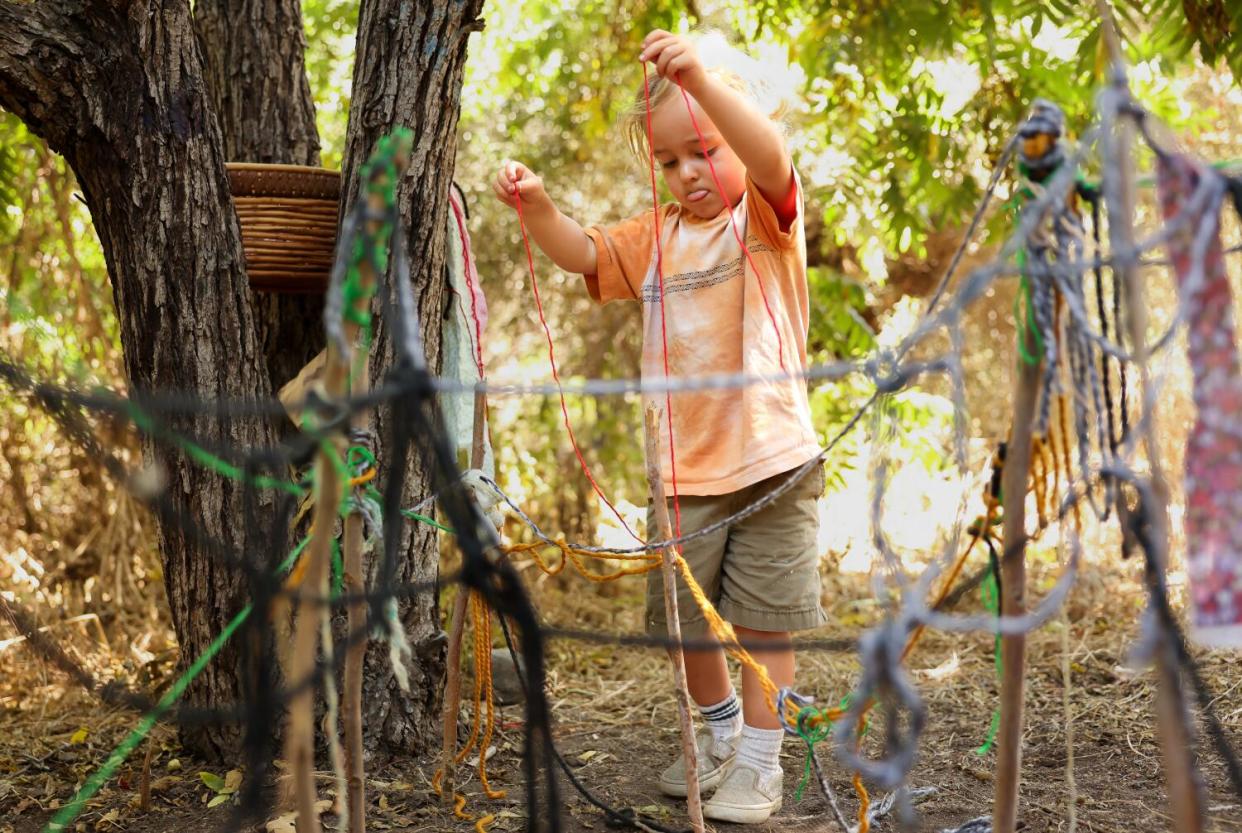 A child plays with a web of yarn and sticks.