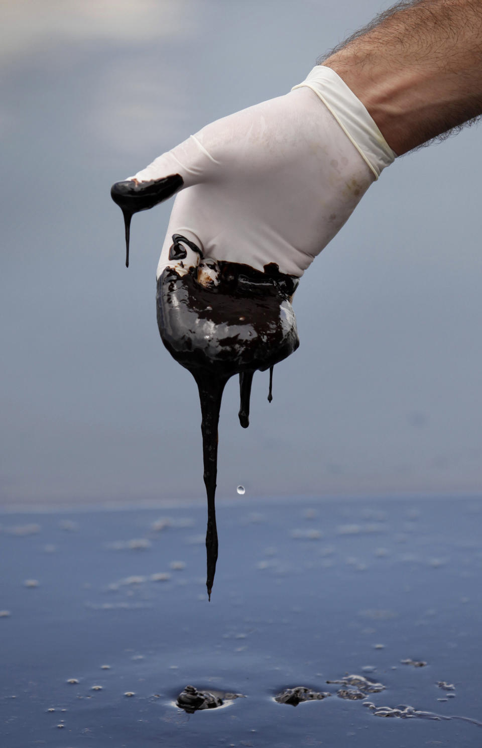 FILE - In this June 15, 2010 file photo, a member of Louisiana Gov. Bobby Jindal's staff wearing a glove reaches into thick oil on the surface of the northern regions of Barataria Bay in Plaquemines Parish, La. Over BP’s objections, a federal appeals court on Friday Jan. 10, 2014, upheld a judge's approval of the company’s multibillion-dollar settlement with lawyers for businesses and residents who claim the massive 2010 oil spill in the Gulf of Mexico cost them money. (AP Photo/Gerald Herbert, File)