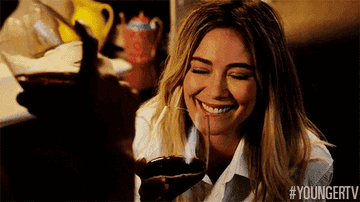 Hilary Duff smiling and raising a glass in a toast, text at bottom #YOUNGERTV