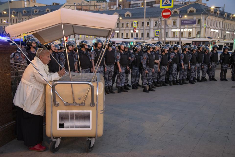 An ice cream seller stands in front of police line blocked protesters during an unsanctioned rally in the center of Moscow, Russia, Saturday, July 27, 2019. Russian police cracked down fiercely Saturday on demonstrators in central Moscow, beating some people and arresting more than 1,000 who were protesting the exclusion of opposition candidates from the ballot for Moscow city council. Police also stormed into a TV station broadcasting the protest. (AP Photo/Alexander Zemlianichenko)