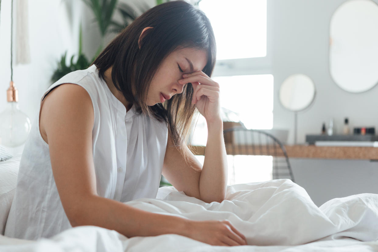 Young woman touching bridge of nose to relieve headache while resting in bed.