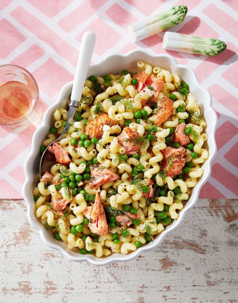 spring pasta with salmon peas and dill in a white scalloped oval serving bowl with a spoon