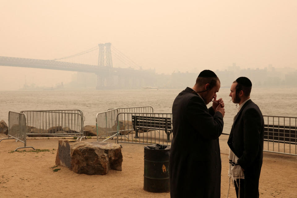 An Orthodox Jewish man lights a cigarette while standing with another by the waterfront as haze and smoke caused by wildfires in Canada cover the Manhattan skyline on June 7, 2023.<span class="copyright">Amr Alfiky—Reuters</span>