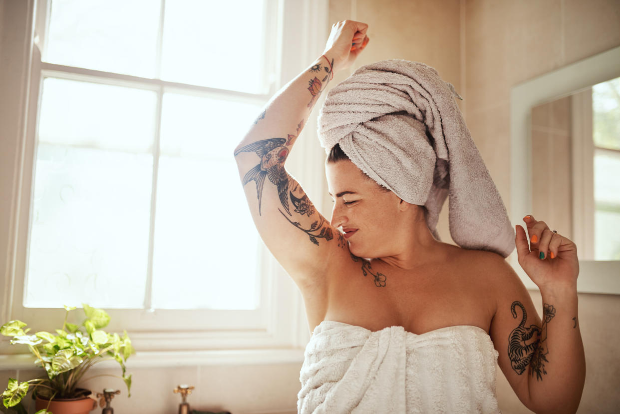 A woman wearing a towel smells her underarm.