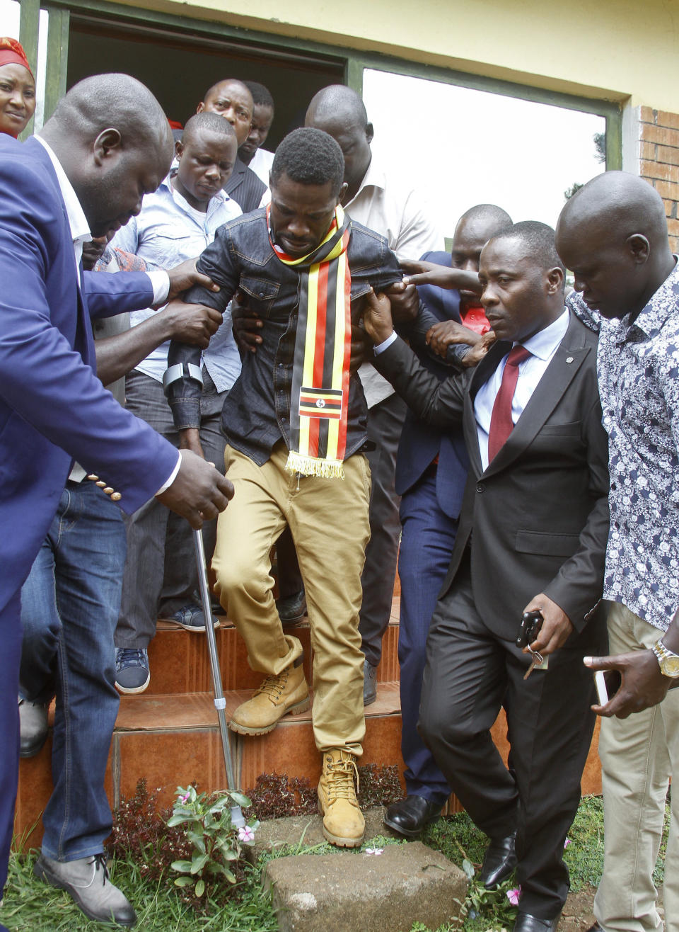 FILE - In this Thursday, Aug. 23, 2018 file photo, Ugandan pop star-turned-lawmaker Kyagulanyi Ssentamu, also known as Bobi Wine, center, is assisted walking on crutches as he is led out of a magistrate's court towards a prison van, in Gulu, northern Uganda. Wine is due to return home on Thursday, Sept. 20, 2018 after seeking treatment in the United States for injuries suffered during alleged state torture. (AP Photo, File)
