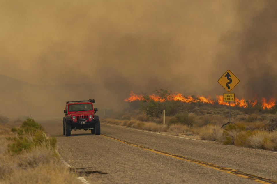 A car passes rising flames from the York Fire on Ivanpah Rd., Sunday, July 30, 2023, in the Mojave National Preserve, Calif. Crews battled “fire whirls” in California’s Mojave National Preserve this weekend as a massive wildfire crossed into Nevada amid dangerously high temperatures and raging winds. (AP Photo/Ty O'Neil)