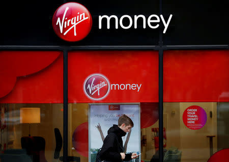 FILE PHOTO: A man checks his phone as he walks past a branch of Virgin Money in Manchester, Britain September 21, 2017. REUTERS/Phil Noble/File Photo