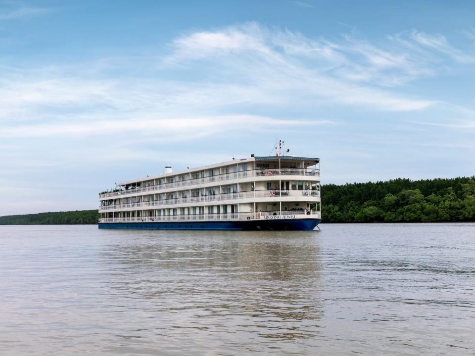 A cruise ship on a body of water with a green hill in the background.