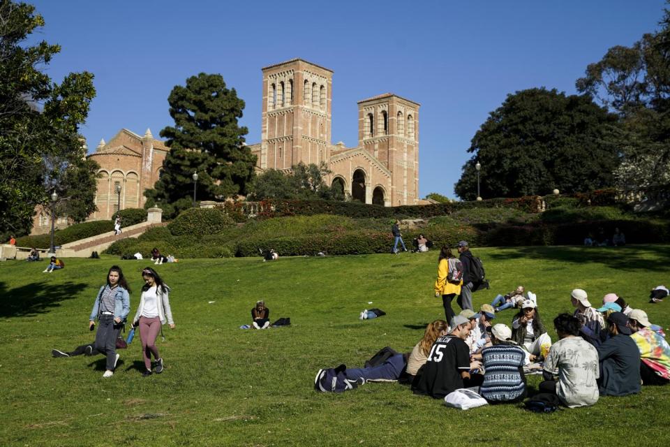 People sit and stroll on a lawn with buildings in the background