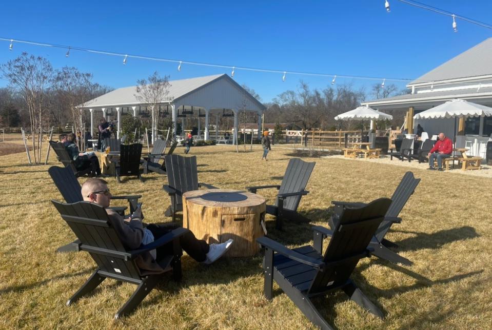 Customers enjoying the outdoor seating around firepits at Tall Oaks Farm + Brewery in Farmingdale. The covered and heated events pavilion can be seen in the background, as well as more outdoor seating areas.