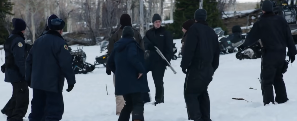 A group of people with guns surrounding one other man in wind wiver