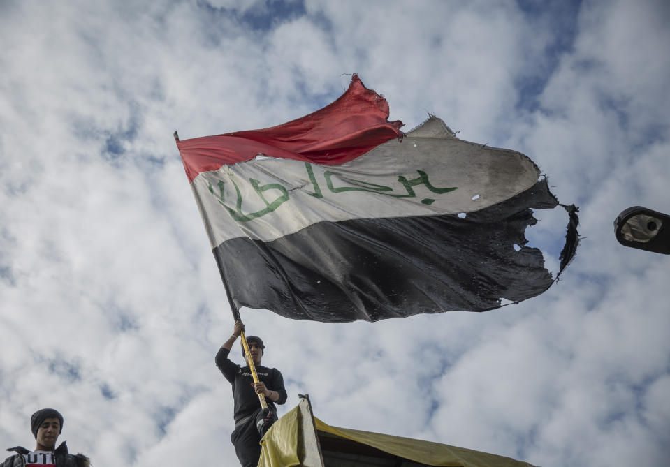 An anti government protester flies an Iraqi flag on top of cement blocks that separate protesters from riot police, during the ongoing protests in Tahrir square, Baghdad, Iraq, Friday, Jan. 10, 2020. (AP Photo/Nasser Nasser)