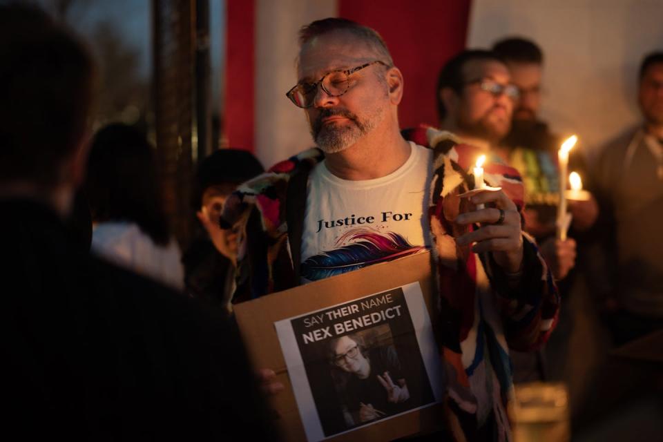 A man holds a candle and has a sign that says, 'Say their name Nex Benedict'