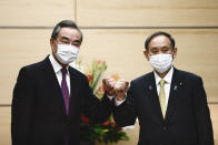 Japan's Prime Minister Yoshihide Suga, right, bumps elbows with China's Foreign Minister Wang Yi at the start of their meeting in Tokyo, Wednesday, Nov. 25, 2020. (Behrouz Mehri/Pool Photo via AP)