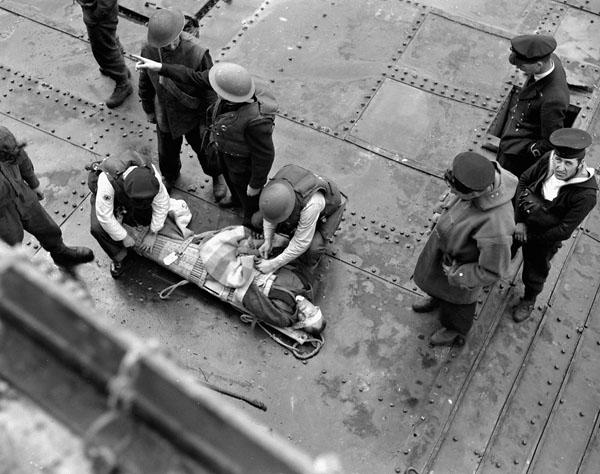 A wounded Canadian soldier being given adrenalin on the deck of a Landing Craft Tank (LCT) alongside H.M.C.S. PRINCE DAVID off the Normandy beachhead, France, 6 June 1944.