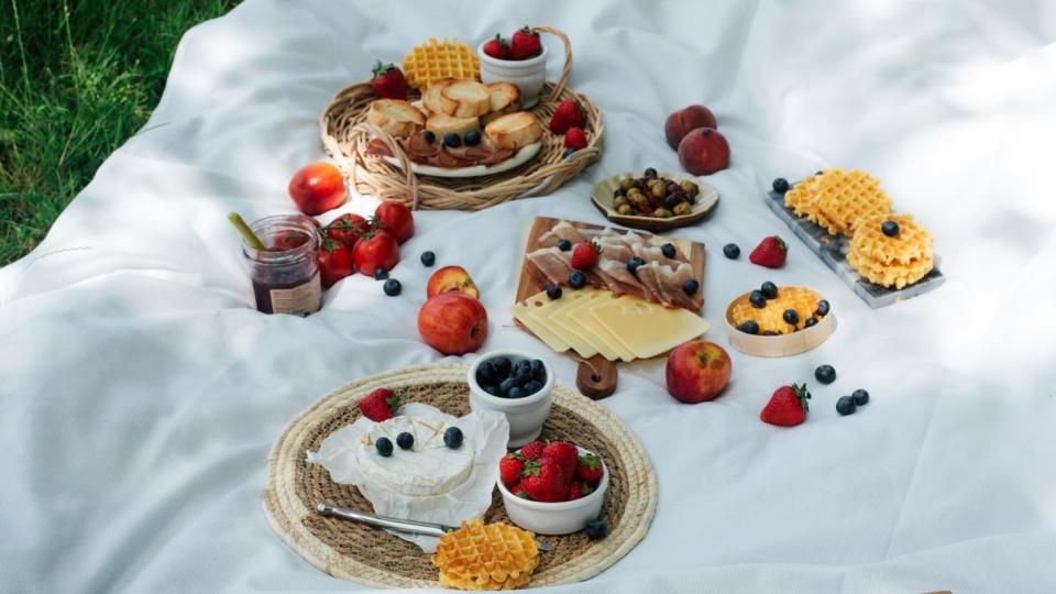 picnic with tasty and healthy food in nature nicely served picnic food in nature fruits, vegetables, cheese, jamon and croutons for a picnic spending time outdoors a white tablecloth or bedspread on the grass top view of a picnic