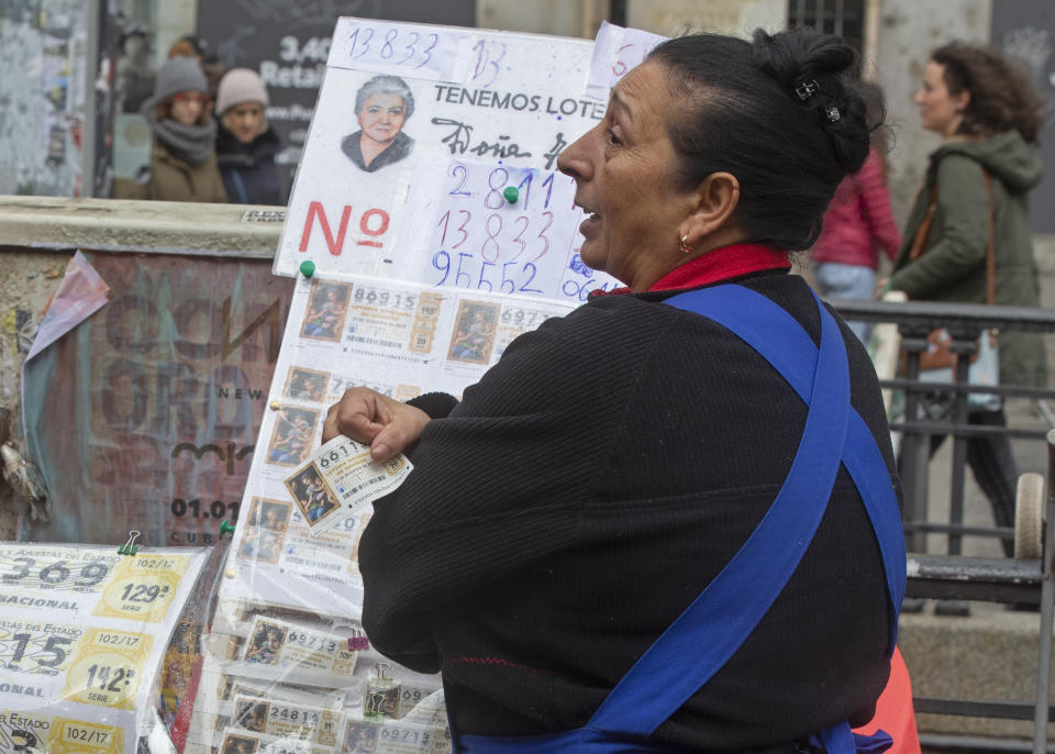 A Christmas lottery seller holds a ticket from her display in Madrid, Spain, Saturday, Dec. 21, 2019. Spain's bumper Christmas lottery draw known as El Gordo, or The Fat One will be held on Dec. 22. (AP Photo/Paul White)