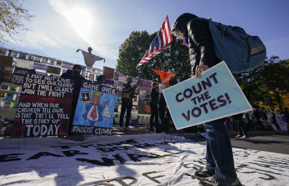 A demonstrator reads a banner on display at Black Lives Matter Plaza, Thursday, Nov. 5, 2020, in Washington. (AP Photo/Alex Brandon)