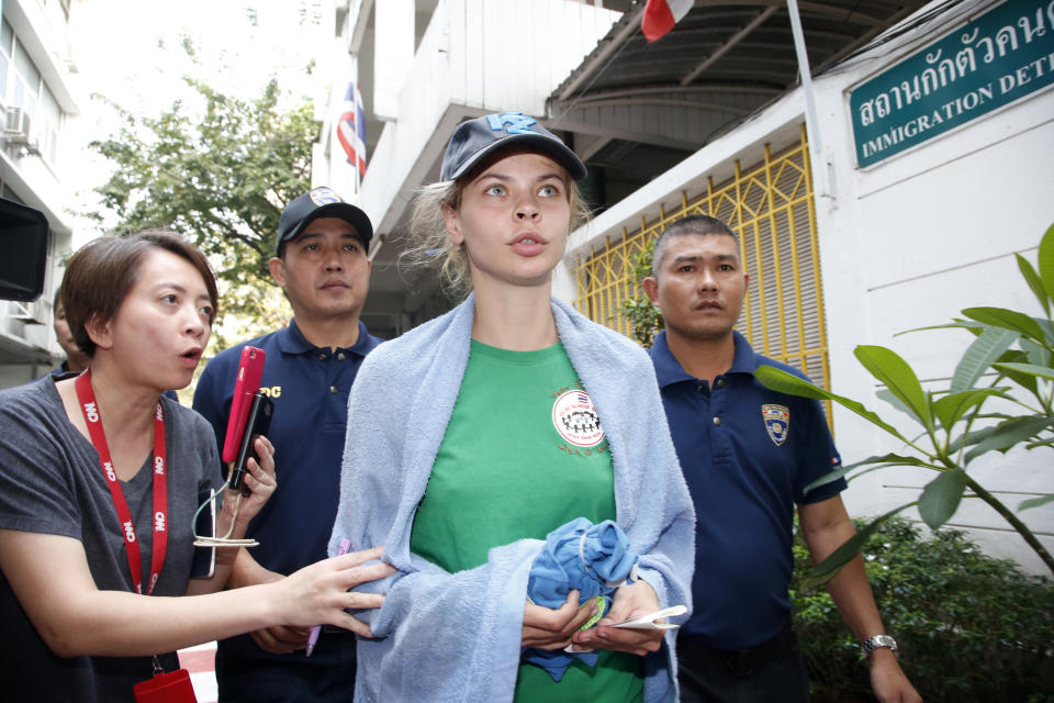 Belarusian model Anastasia Vashukevich, center, speaks to journalists while being escorted by Thai Immigration police officers from the Immigration Detention Center towards a vehicle to take her to an airport for deportation in Bangkok, Thailand, Thursday, Jan. 17, 2019. Thai officials say they are deporting Vashukevich who claimed last year that she had evidence of Russian involvement in helping elect Donald Trump president. (AP Photo/Sakchai Lalit)