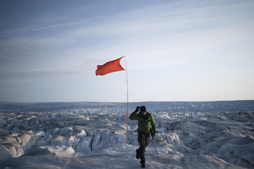 In this Aug. 16, 2019, photo, Brian Rougeux, NYU Field Safety Officer, walks after installing a flag to help identify a GPS position at the Helheim glacier, in Greenland. Summer 2019 is hitting the island hard with record-shattering heat and extreme melt. Scientists estimate that by the end of the summer, about 440 billion tons of ice, maybe more, will have melted or calved off Greenland's giant ice sheet. Helheim glacier has shrunk about 6 miles (10 kilometers) since scientists visited in 2005. (AP Photo/Felipe Dana)