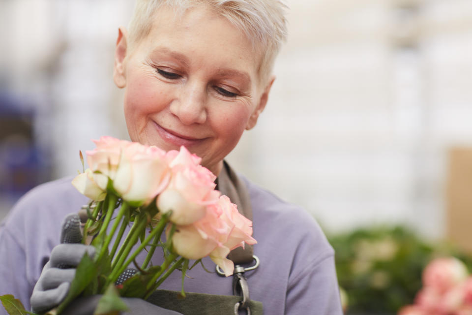 Mature gardener with short hair holding roses in her hands and smelling them