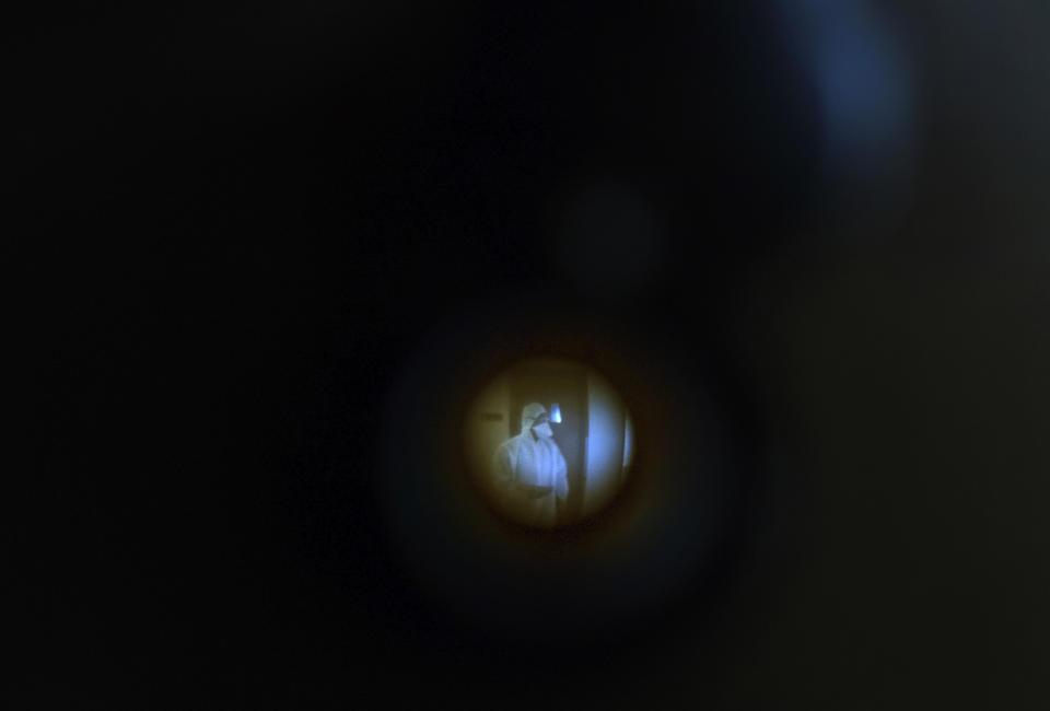 A civic worker is seen through the peephole of Associated Press photographer Rafiq Maqbool's room, as he waits to fill a swab test form for the photographer, at the hotel where Maqbool is in quarantine in Mumbai, India, April 24, 2020. Maqbool was tested positive for COVID-19 with dozens of other journalists, who were then moved collectively to a hotel turned quarantine center. He left his wife and children home alone to deal with a sealed building, anxious relatives and the stigma of being related to someone who had caught the virus. On the seventh day, the test from his second swab test turned out negative and he was allowed to return home to be under home quarantine for 14 days. (AP Photo/Rafiq Maqbool)