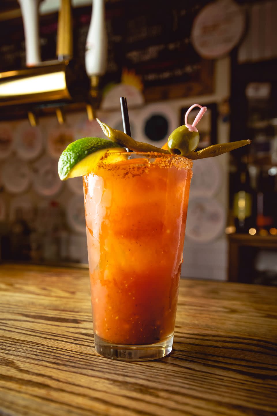 a tall cool back lit bloody mary drink sits on a wood bar counter vertical
