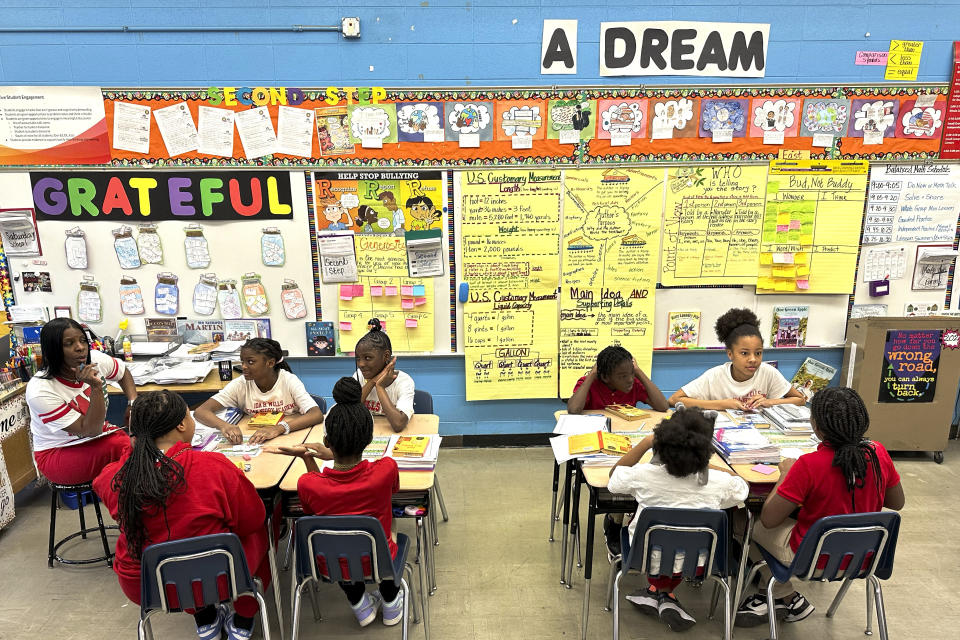 Wells Preparatory Elementary School teacher Charlotte Owens, left, works with her fifth grade students during the literature segment of their day, Friday, March 8, 2024, in Chicago. In Chicago Public Schools, the average reading score went up by the equivalent of 70% of a grade level from 2022 to 2023. Math gains were less dramatic, with students still behind almost half a grade level compared to 2019. Chicago officials credit the improvement to changes made possible with nearly $3 billion in federal relief. (AP Photo/Charles Rex Arbogast)