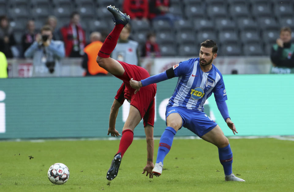 Marvin Plattenhardt, del Hertha Berlín observa el balón, mientras cae Janik Haberer, del Friburgo, durante un encuentro de la Bundesliga realizado el domingo 21 de octubre de 2018 (Jens Buettner/dpa via AP)