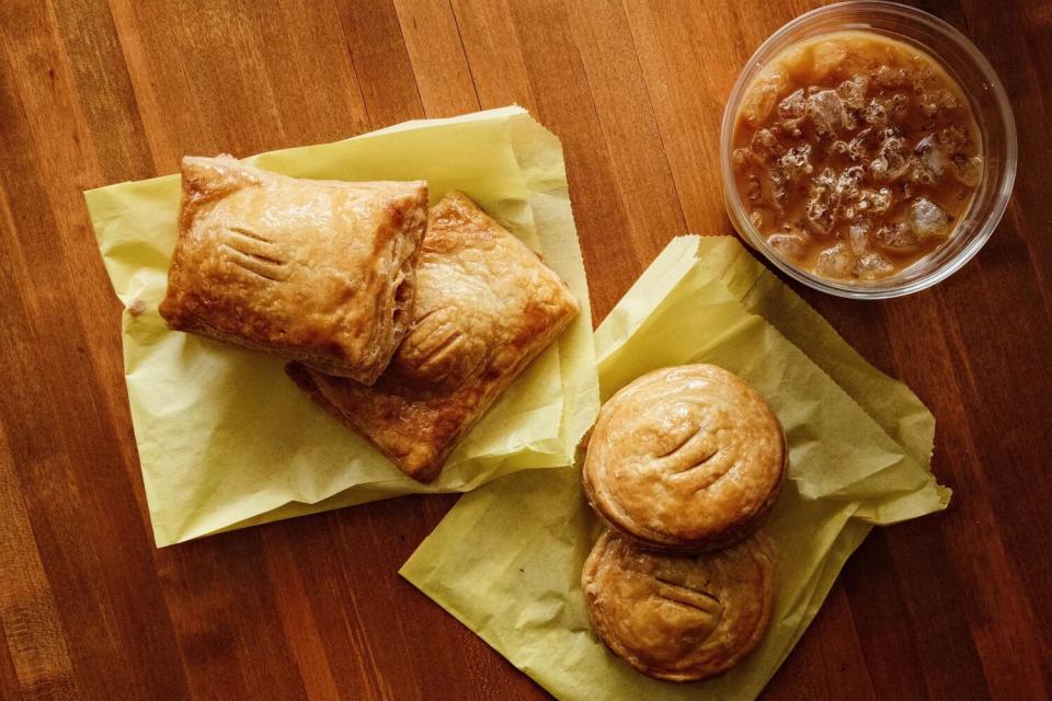 An overhead of four sweet and savory pastelitos atop yellow bags, with an iced cafe con leche, on a tabletop at Cafe Tropical