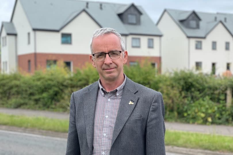 Man with glasses in grey suit in front of new housing estate