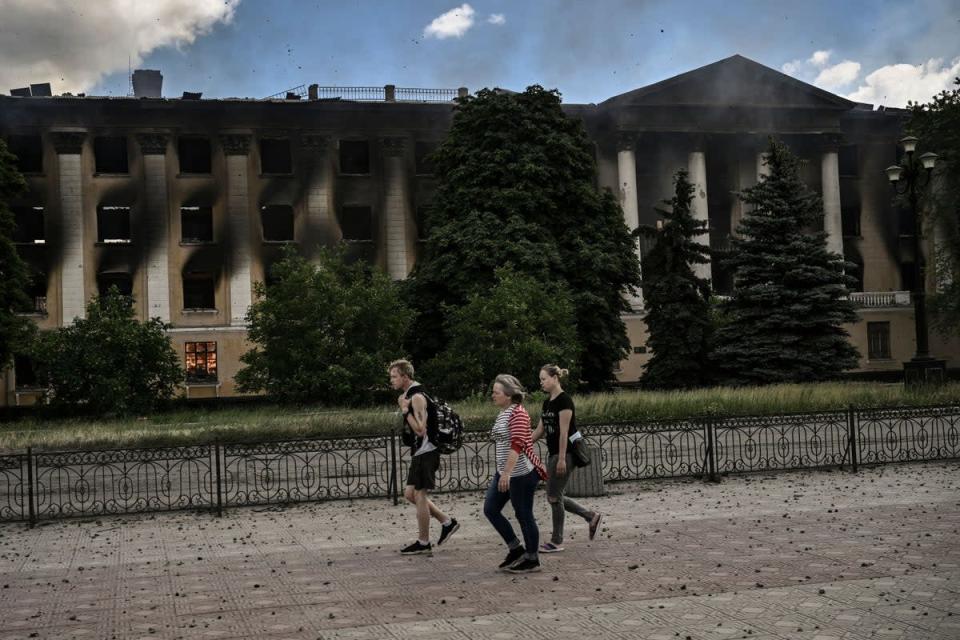 Local residents walk past a burning college after a strike in Lysychansk (AFP via Getty Images)