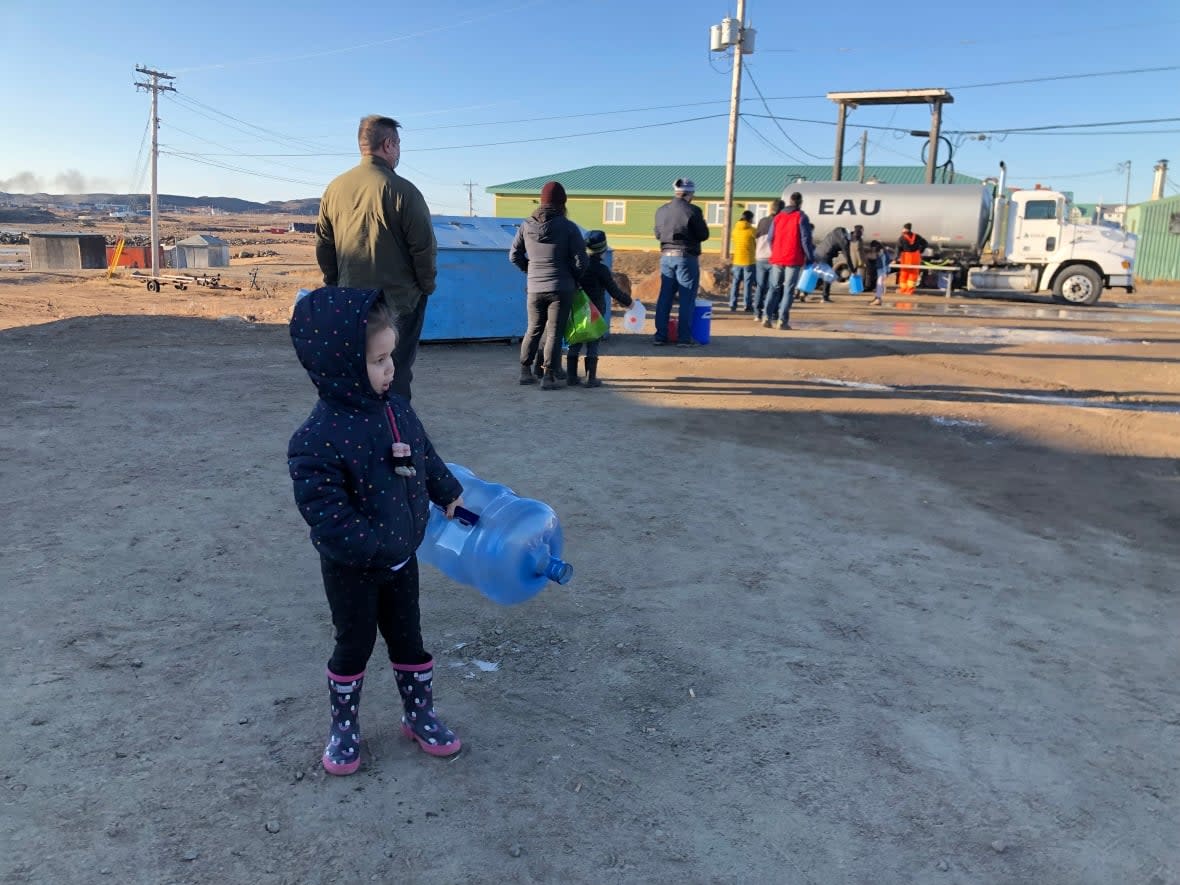 Taylor Matchett's three-year-old daughter, Declan, waits in line at a water distribution point with a refillable water jug in Iqaluit. Matchett said her husband had to pay $32 for a case of bottled water at the start of the crisis, but water has become more 'readily available' in the past few days.  (Submitted by Taylor Marchett - image credit)