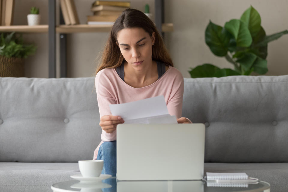 Upset woman sitting on couch at home near computer holding paper reading bad news notification about job rejection, public utility debt, credit refusal letter student failed exam, scholarship concept