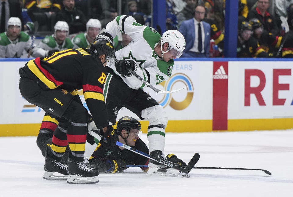 Dallas Stars' Roope Hintz, right, vies for the puck against Vancouver Canucks' Teddy Blueger, bottom, and Dakota Joshua, left, during the second period of an NHL hockey game Thursday, March 28, 2024, in Vancouver, British Columbia. (Darryl Dyck/The Canadian Press via AP)