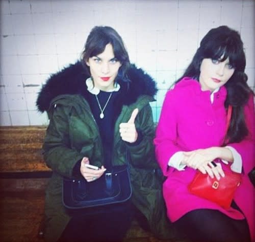 Alexa Chung and Zooey Deschanel cozy up on a subway bench in their brightly-colored coats.