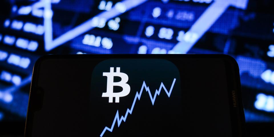 In this photo illustration a Bitcoin logo seen displayed on a smartphone with the stock market graphic in the background