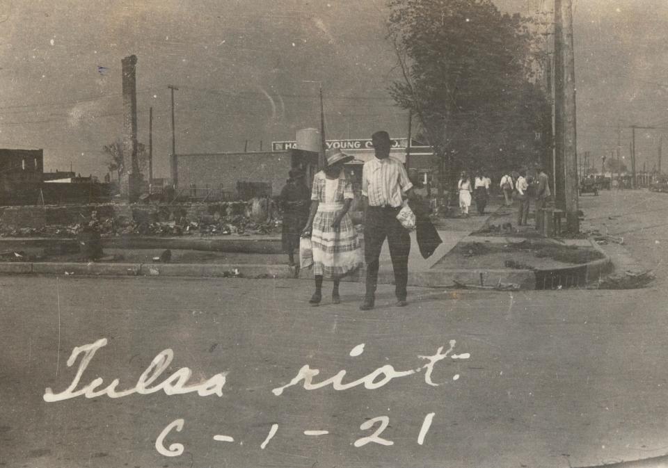 The skyline is dense with smoke as a couple walks across a street in the Greenwood District in June 1921.