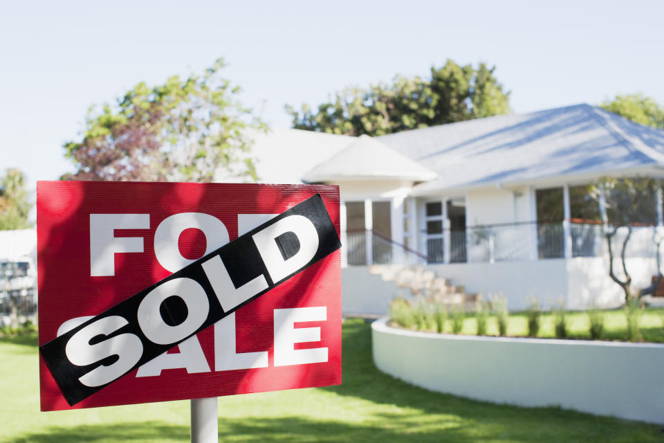 Black "Sold" stamped over a red "For Sale" sign in front of a house