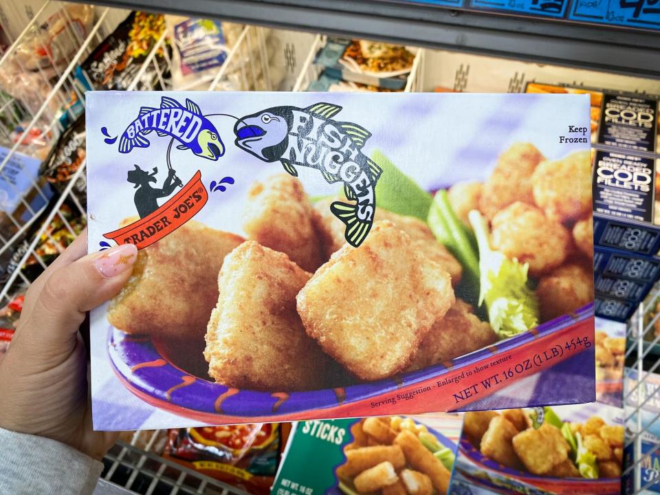 hand holding box of fish nuggets in the frozen aisle at trader joes