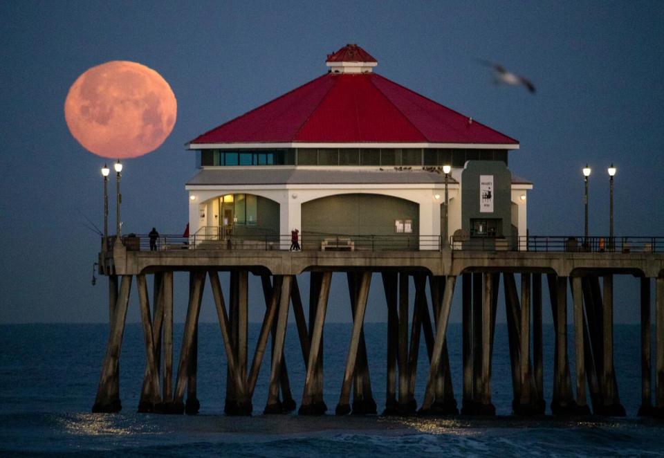 A full moon rises over Huntington Beach Pier at dawn.